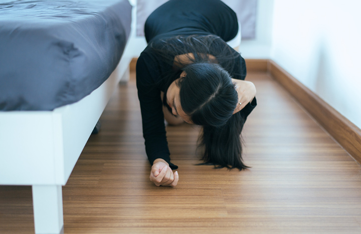 Woman looking under her bed for her lost glasses