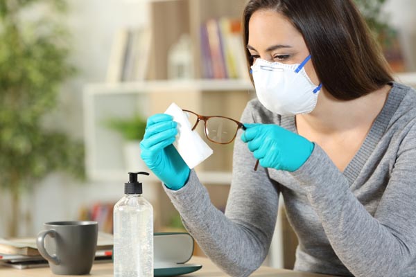 Optician wearing PPE cleaning glasses