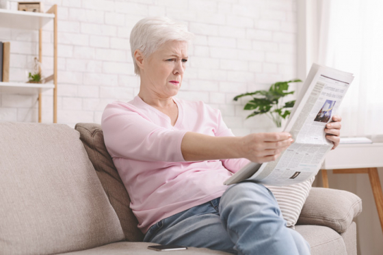 Woman struggling to see newspaper text due to presbyopia